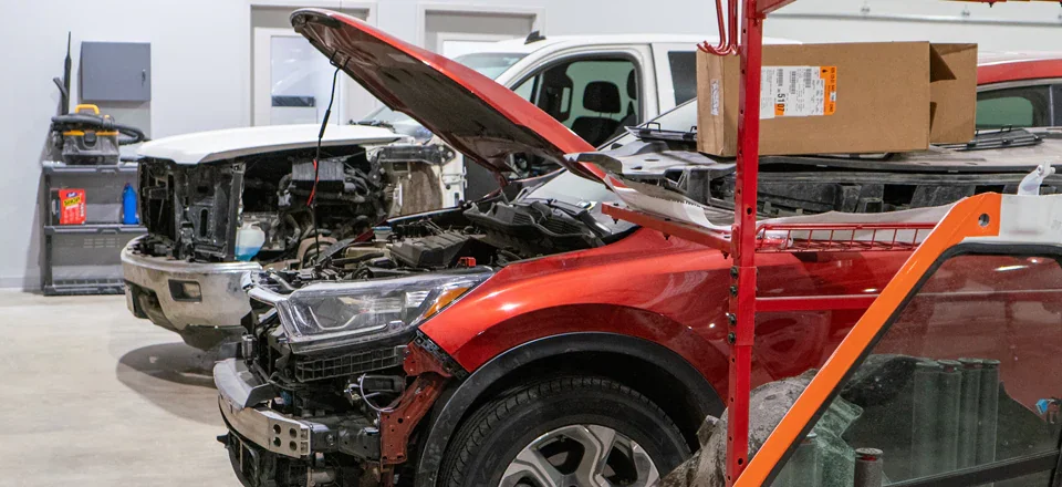 A garage with two partially disassembled cars, one red and one white, both missing front body components.