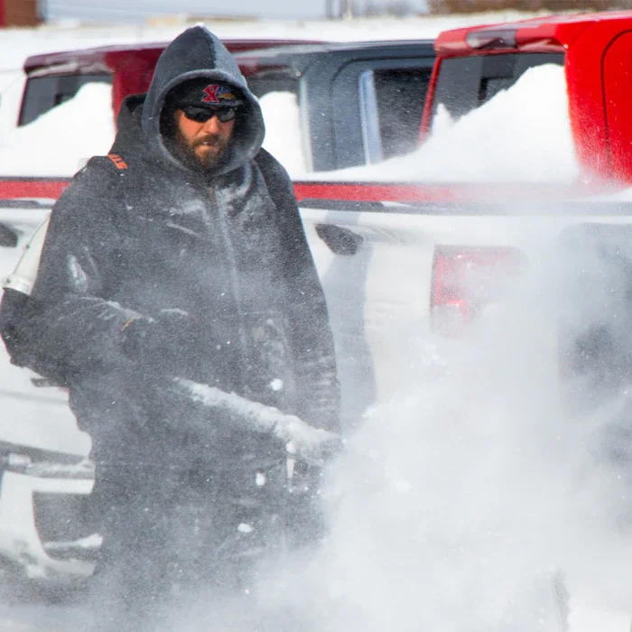 Worker clearing snow from dealership vehicles during winter weather conditions.
